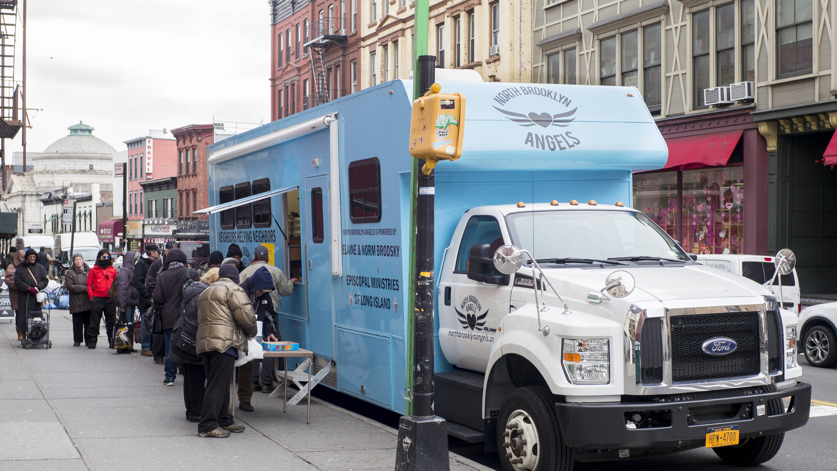 People lined up on the sidewalk at the food truck waiting for food in Brooklyn, NY.